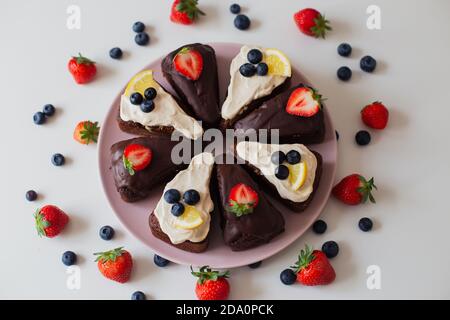 Deliziosa torta al cioccolato fatta in casa con crema di cioccolato e bianco decorata con bacche fresche e fette di limone e tagliate a pezzetti Foto Stock