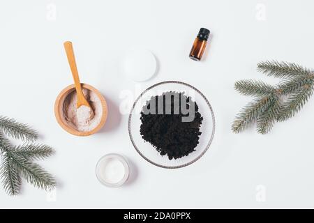 Ingredienti per la pulizia del corpo del caffè su un tavolo bianco accanto ai rami di abete, layout piatto per la cura della pelle invernale. Foto Stock