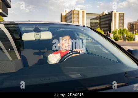 Attraverso la finestra di riflessivo focalizzato giovane afroamericana guida femminile automobile sulla strada Foto Stock