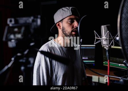 Cantante maschile sicuro in studio di registrazione musicale e di ripresa video su fotocamera professionale per blog Foto Stock