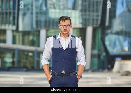 Giovane uomo d'affari serio in abbigliamento formale e orologio da polso in piedi con mani in tasca mentre si guarda la fotocamera Foto Stock