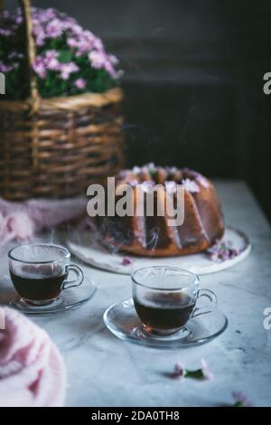 Angolo alto di tè caldo in tazze di vetro disposte sopra Tavolo con deliziosa torta Bundt al limone Foto Stock