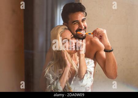 Bell'uomo bearded abbracciando allegra ragazza mentre sfregava i denti insieme in bagno al mattino Foto Stock