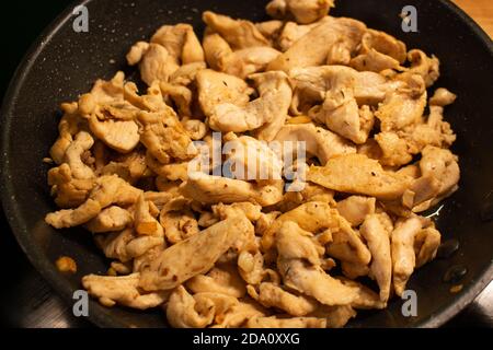 Pezzi di filetto di pollo in una padella nera, piccoli pezzi di carne di pollo tagliati a fette sottili per cucinare Foto Stock