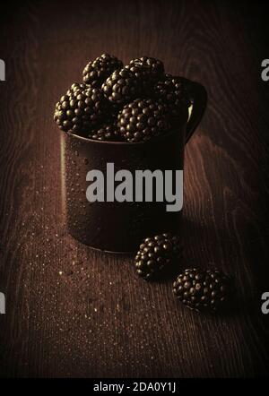 Bacche nere fresche e succose in tazza nera con texture sovrapposte Foto Stock