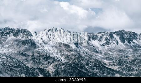 Maestoso scenario panoramico di aspro pendii rocciosi della montagna dei Pirenei Range coperto di neve sotto il cielo nuvoloso in El Pas De la Casa Foto Stock