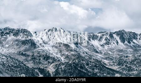 Majestic panoramic scenery of rough rocky slopes of Pyrenees mountain range covered with snow under cloudy sky in El Pas de la Casa Foto Stock