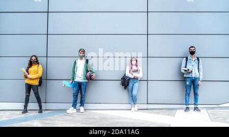 Studenti moderni. Gruppo di diversi adolescenti con maschera facciale in divaricamento sociale in posa con gadget e libri, panorama con spazio vuoto - Nuova normalità Foto Stock