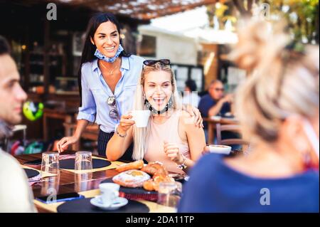 Gruppo di amici felici che hanno fatto colazione nel ristorante con Maschere facciali nel tempo del coronavirus - nuovo stile di vita normale concetto con la gente felice hav Foto Stock