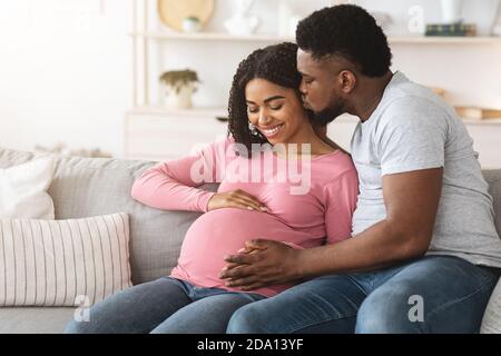 L'uomo nero baciando la sua felice moglie incinta Foto Stock