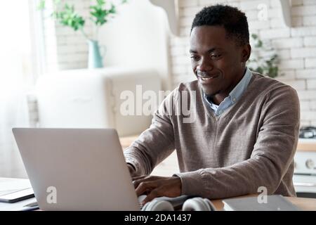 Sorridente afroamericano che usa un computer portatile che lavora da casa. Foto Stock