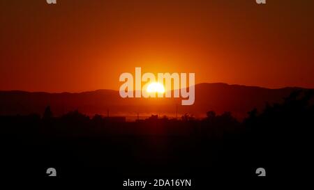 Tramonto mozzafiato con sole luminoso che illumina il paesaggio in colori rosso e arancione sopra la città deserta Merzouga, nel sud del Marocco, Africa. Foto Stock