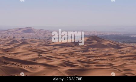 Splendida vista panoramica sulle grandi dune di sabbia del deserto Erg Chebbi con villaggio Merzouga, Marocco, Africa al sole di mezzogiorno con aria frizzante. Foto Stock