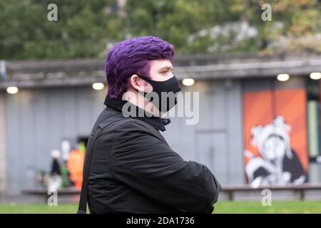 Giovane uomo con capelli viola che indossa maschera nera al di fuori, osservando la protesta anti-blocco Manchester 08-11-2020, covid, covid19, 2020 Foto Stock