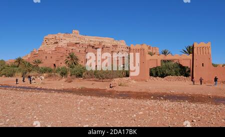 I turisti scattano foto con un cammello sotto lo storico ksar Ait Benhaddou moresco, sito patrimonio dell'umanità dell'UNESCO, con edifici storici a forma di cammello. Foto Stock