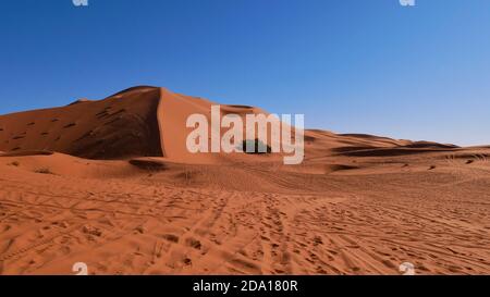 Enorme duna di sabbia ben formata con tracce viste dal basso in Erg Chebbi vicino a Merzouga, Marocco, Africa in giornata di sole con cielo blu. Foto Stock