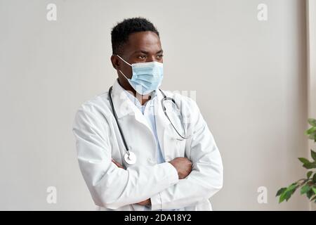 African nero maschio medico indossando maschera facciale guardando via isolato su bianco. Foto Stock