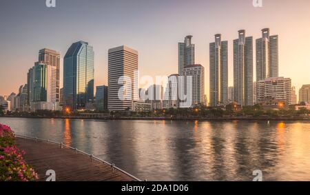 Grattacieli e lago con passeggiata in legno nel parco cittadino. Vista del parco Benjakiti all'alba. Bella scena mattutina del Parco pubblico a Bangkok, Thailandia Foto Stock