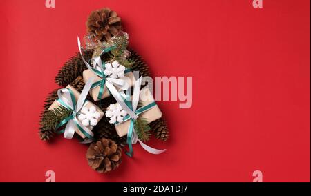 Albero di Natale alternativo fatto di regali e coni di albero su un rosso. Spazio per i desideri. Tessera vacanze. Vista dall'alto. Felice Anno Nuovo. Foto Stock