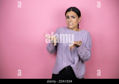 Bella donna che indossa un maglione viola casual su sfondo rosa disgustava l'espressione, dispiaciuto e pauroso fare faccia disgusto perché avversione Foto Stock