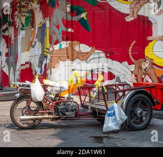 La moto da carico parcheggiata in un angolo di strada a Soi Na Na, Chinatown, Bangkok con un muro coperto di graffiti dietro di esso. Foto Stock