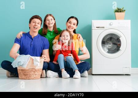 L'uomo, la donna e le ragazze dei bambini piccoli aiutanti stanno avendo divertimento e sorridente mentre facendo il bucato a casa. Foto Stock