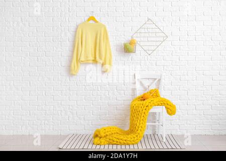 Sedia con plaid giallo e filo da maglieria vicino mattone bianco parete Foto Stock