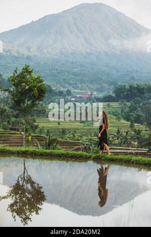 Donna che cammina contro le fantastiche terrazze di riso di Jatiluwih a Bali. Bellezza e armonia nella natura. Indossabile in un lungo abito nero. Foto Stock