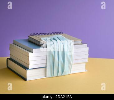 Libri impilati legati con maschera facciale. Ritorno a scuola durante il concetto di coronavirus. Foto Stock