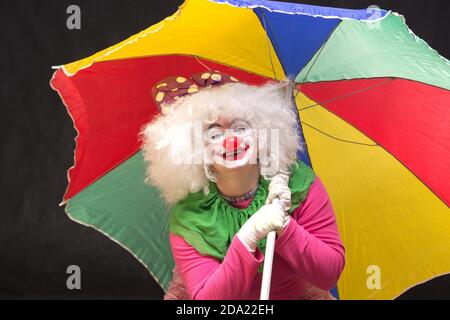 Jolly buon clown divertente con un ombrello multicolore su un sfondo nero Foto Stock