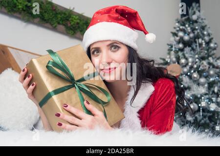 Ritratto di una donna felice in tessuto di babbo natale abbracciando molte scatole regalo sullo sfondo decorato per appartamento di Natale. Ragazza con regalo di Natale Foto Stock