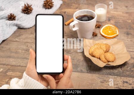 Immagine mockup delle mani di donna che tengono cellulare con schermo vuoto sul tavolo in caffetteria. Telefono cellulare in mani femminili Foto Stock