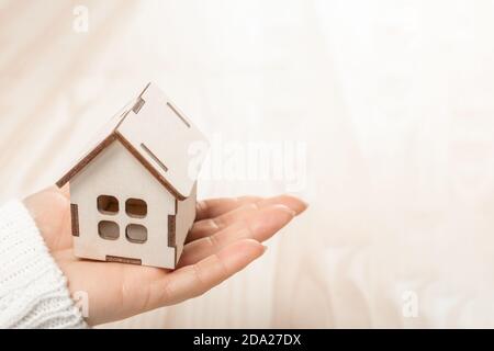 Modello di casa giocattolo di legno in mano di donna su sfondo di legno. Mano tiene un piccolo modello di una casa di legno. Foto Stock