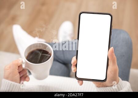 Immagine mockup di donna che tiene nero telefono cellulare con schermo bianco vuoto in caffetteria. Inquadratura ritagliata dello smartphone con le mani della donna e co vuoto Foto Stock