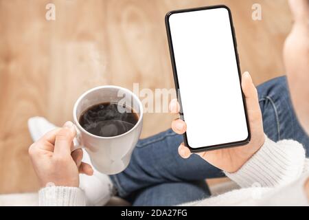 Immagine mockup di una donna che tiene il telefono cellulare con schermo bianco vuoto con tazza da caffè. Cellulare Mockup immagine schermo bianco vuoto. Sfondo vuoto spa Foto Stock