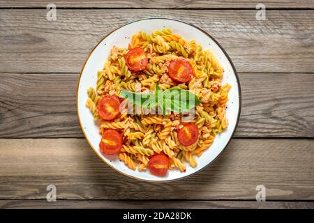 Fusilli - classica pasta italiana di grano duro con carne di pollo, pomodori ciliegia, basilico in salsa di pomodoro in ciotola bianca su tavola di legno mediterranea Foto Stock