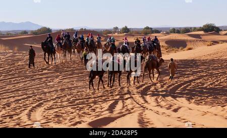 Merzouga, Marocco - 12/30/2019: I turisti che si godono un giro in cammello dromedario nelle dune di sabbia di Erg Chebbi, una popolare destinazione turistica. Foto Stock