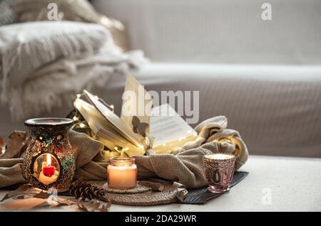 Candele in candele, libro, maglione, ghirlanda sullo sfondo luminoso del soggiorno. Home autunno concetto Foto Stock