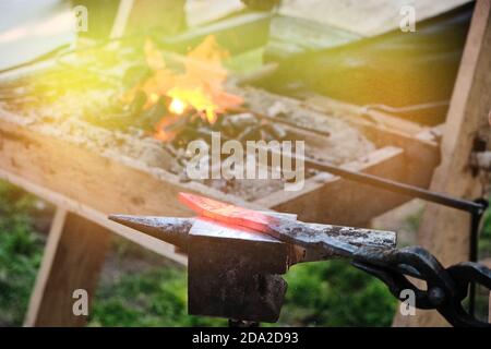 Lama calda sull'incudine. Pezzo nella forgia sullo sfondo del fuoco. Il calore dalla stufa e la lama della spada forgiata. Foto Stock