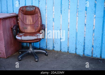 Shabby vecchia sedia esecutiva in pelle, concetto di problemi finanziari. Parete blu con posizione per il testo, spazio per la copia Foto Stock