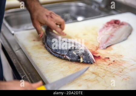 Chef pulizia orata in cucina. Uno Chef in un taglia il pesce. Ancora vita sulla tavola della cucina. Cibo abbondante per le regioni fredde. Foto Stock