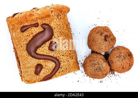 Il cioccolato fatto a mano viene cosparso di cacao. Caramelle al cioccolato e rotolo - vista dall'alto, isolate su sfondo bianco. Rotolo e caramella bevendo con cioccolato. Foto Stock