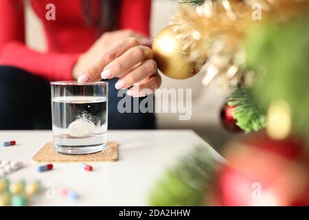 Donna gettando la pillola solubile effervescente in vetro di acqua a. casa vicino closeup albero di natale Foto Stock