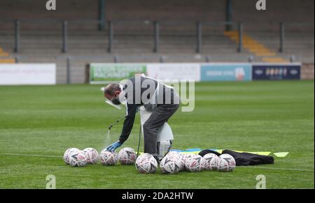 Un ufficiale che indossa DPI spruzzerà palloni con spray disinfettante prima del primo round della fa Cup Emirates tra Torquay United e Crawley Town a Plaimoor, Torquay. Foto James Boardman / Telephoto Images Foto Stock