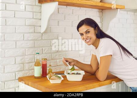 Ritratto della donna felice che mangia insalata per pranzo e cibo da asporto consegnato dal servizio di consegna. Foto Stock