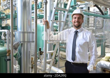 Ritratto di un successo imprenditore sorridente/ tecnico sul sito in uno stabilimento industriale con casco Foto Stock