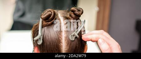 Vista posteriore della mano del parrucchiere che fa taglio di capelli di giovani donna con capelli clip sui capelli in parrucchiere Foto Stock