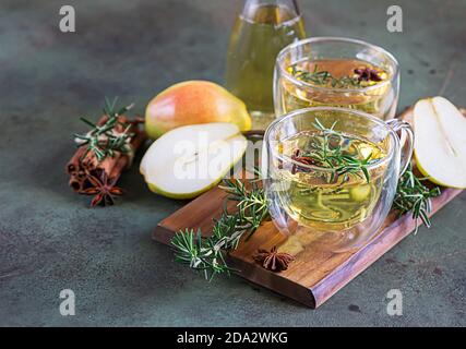 Tazze di vetro con pera calda o sidro di mela per Natale o Capodanno. Bevanda tradizionale autunnale o invernale con rosmarino, cannella e anice. Calcestruzzo verde Foto Stock