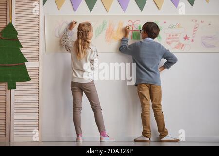 Vista posteriore a tutta lunghezza su ragazzo e ragazza che disegnano sulle pareti mentre si gode la lezione d'arte a scuola, spazio di copia Foto Stock