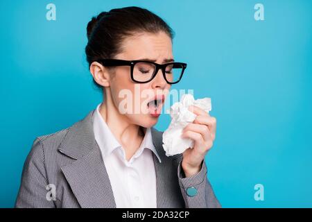 Primo piano ritratto di attraente insegnante di signora malata starnuti di influenza utilizzando un tovagliolo isolato su uno sfondo di colore blu brillante Foto Stock